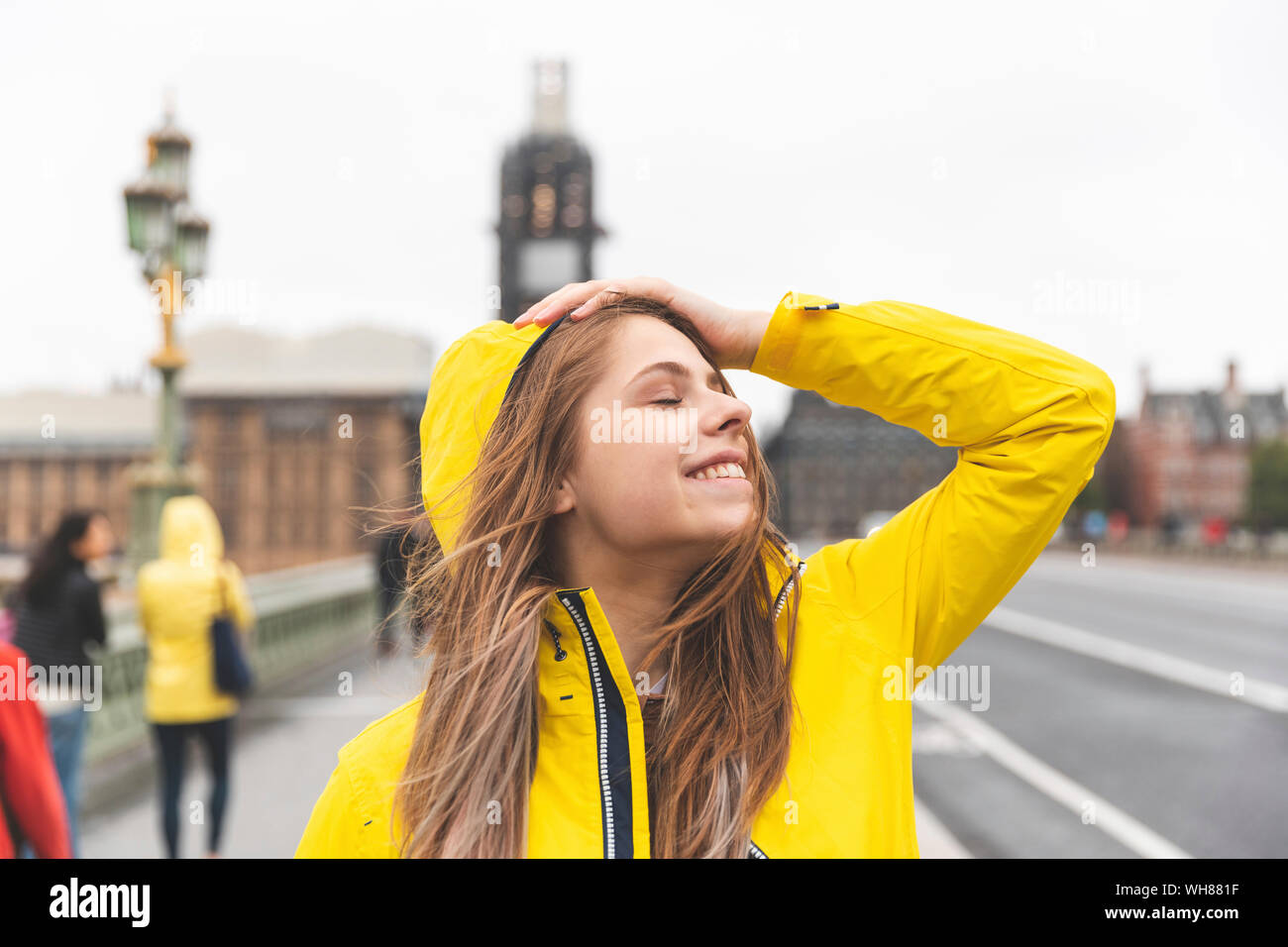 Glückliche junge Frau tragen gelbe Regenmantel an einem regnerischen Tag, London, UK Stockfoto