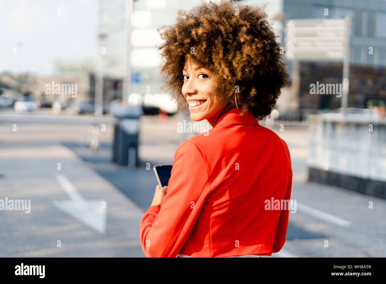 Portrait von lächelnden jungen Frau mit Smartphone das Tragen modischer roten Anzug Jacke Stockfoto