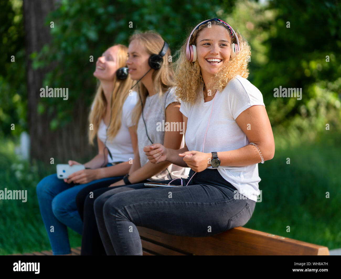 Drei junge Frauen Musik hören mit Kopfhörern und Smartphones auf eine Rückenlehne der Rücksitzbank Stockfoto