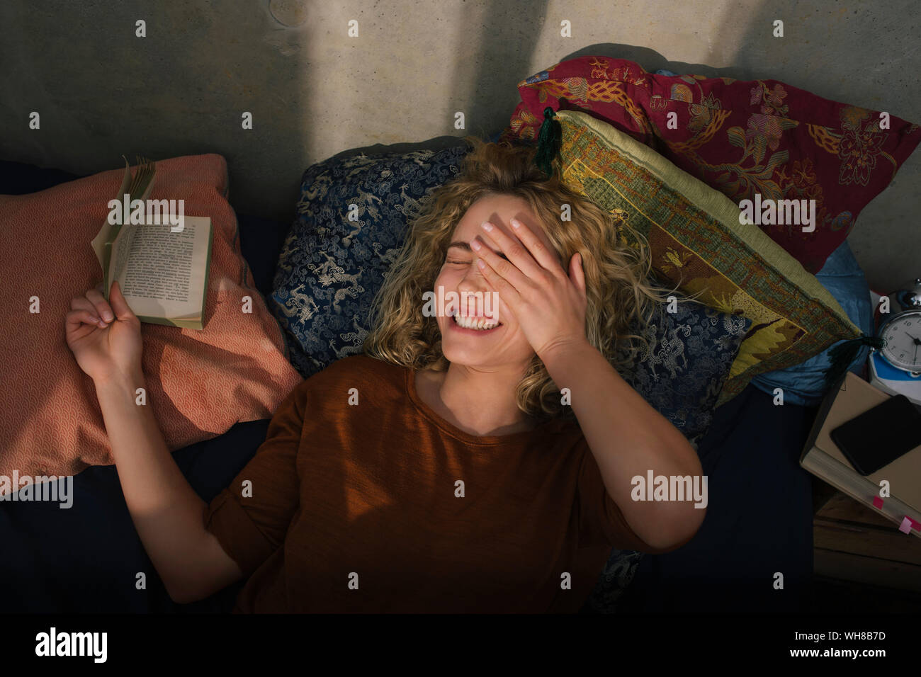 Portrait von Lachende junge Frau auf dem Bett liegen, ein Buch lesen Stockfoto