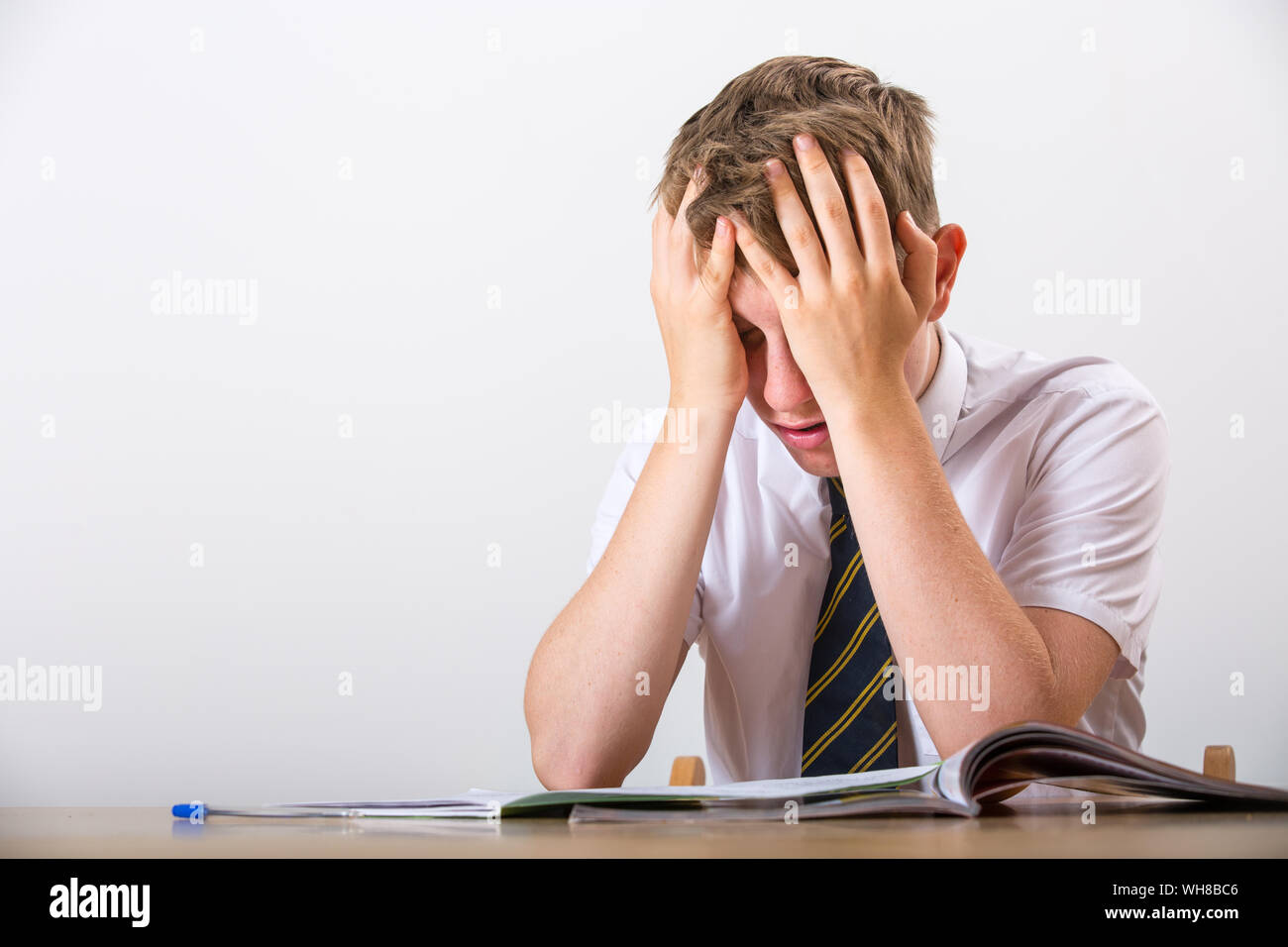 Ein gestresster Schüler mit dem Kopf in seinen Händen saß an seinem Schreibtisch Stockfoto