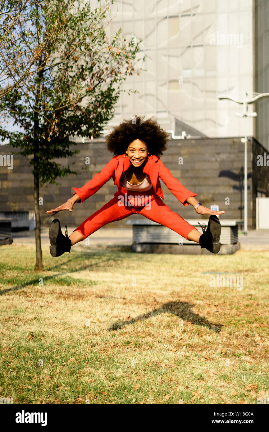 Porträt der glückliche junge Frau mit modischen roten Hosenanzug springen in die Luft, Stockfoto