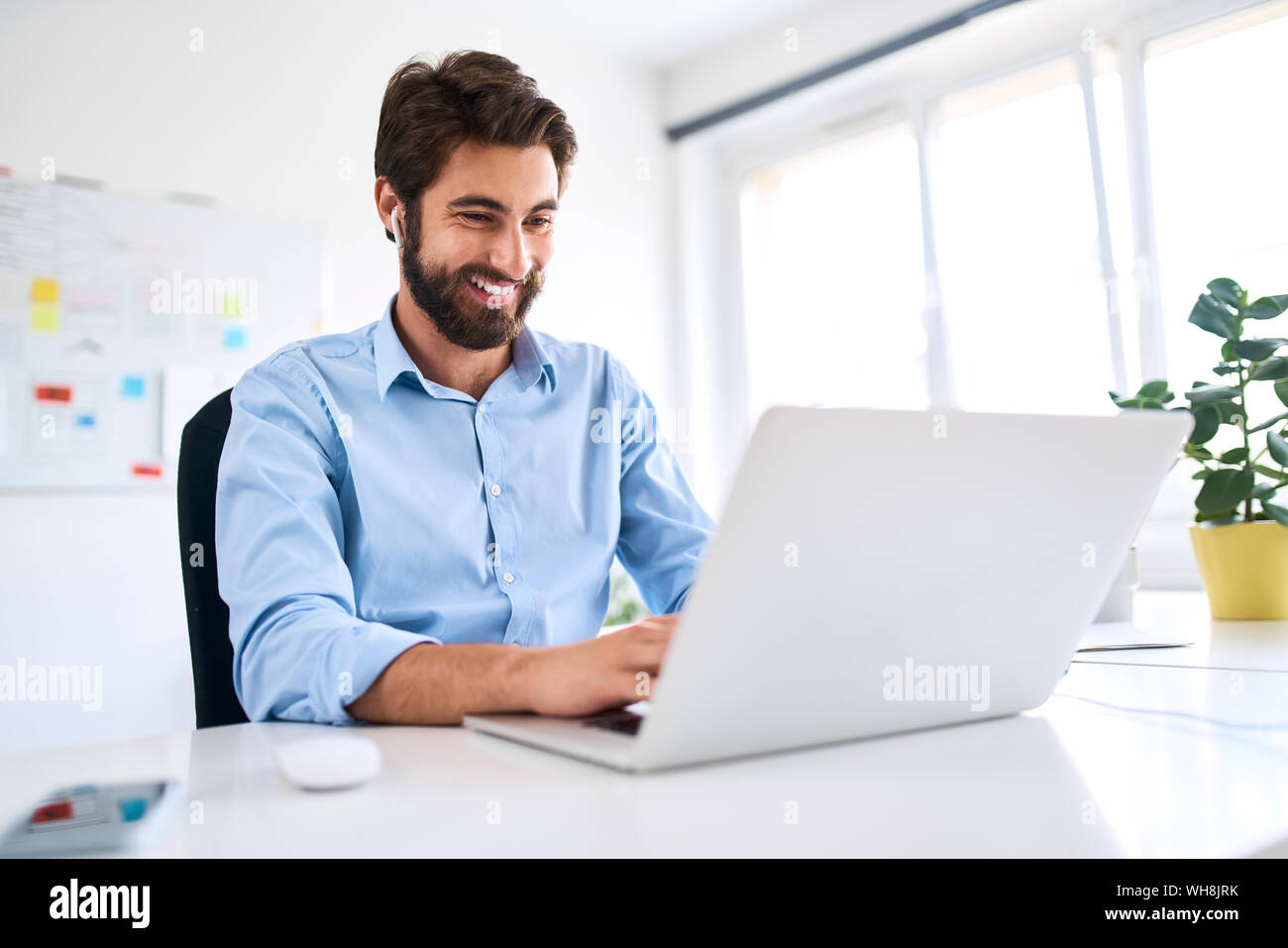 Lächelnd Geschäftsmann mit Kopfhörer an einem Schreibtisch mit einem Laptop Stockfoto