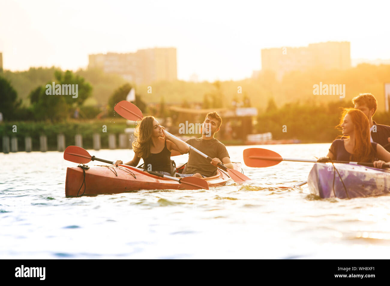 Glückliche Junge kaukasier Gruppe von Freunden Kajakfahren auf dem Fluss mit Sonnenuntergang im Hintergrund. Spaß in der Freizeit. Gerne männliche und weibliche Modell laughting auf dem Kajak. Sport, Beziehungen Konzept. Stockfoto