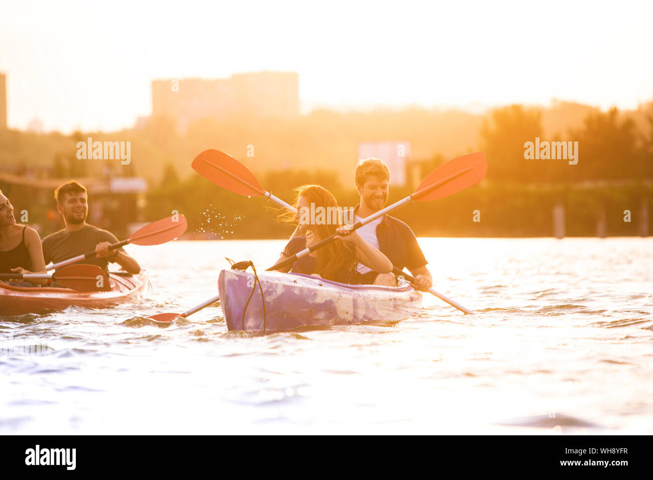 Glückliche Junge kaukasier Gruppe von Freunden Kajakfahren auf dem Fluss mit Sonnenuntergang im Hintergrund. Spaß in der Freizeit. Gerne männliche und weibliche Modell laughting auf dem Kajak. Sport, Beziehungen Konzept. Stockfoto