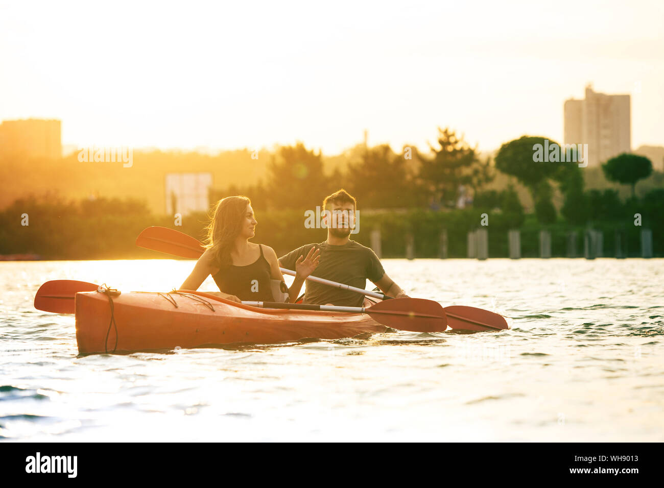 Selbstbewussten jungen kaukasischen Paar Kajakfahren auf dem Fluss zusammen mit Sonnenuntergang im Hintergrund. Spaß in der Freizeit. Romantisch und glückliche Frau und Mann auf dem Kajak. Sport, Beziehungen Konzept. Stockfoto