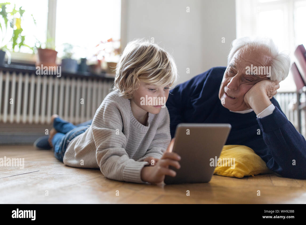 Großvater und Enkel zu Hause auf dem Boden liegend mit einem Tablet Stockfoto