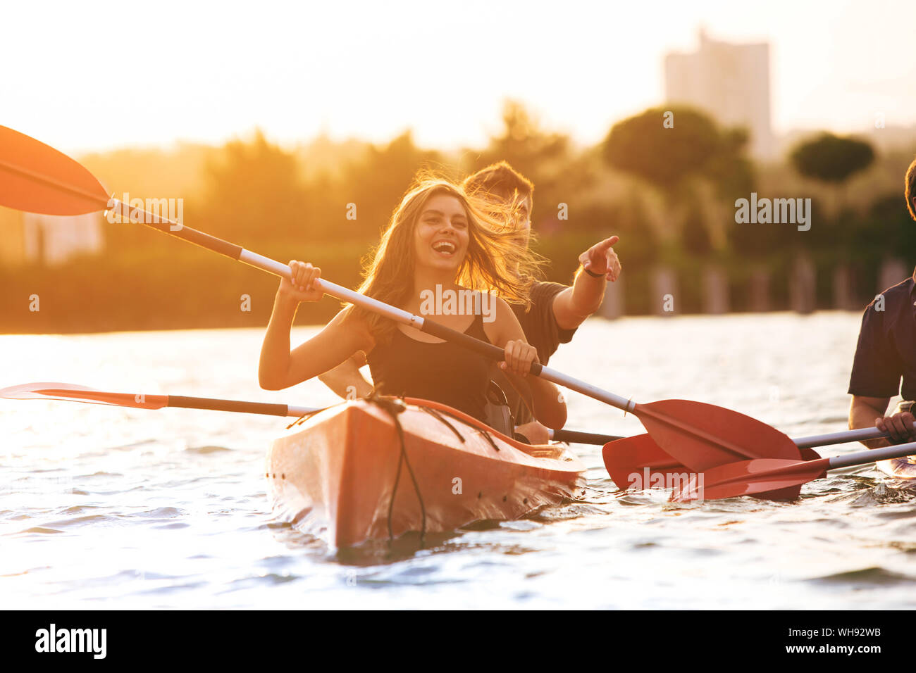 Selbstbewussten jungen kaukasischen Paar Kajakfahren auf dem Fluss zusammen mit Sonnenuntergang im Hintergrund. Spaß in der Freizeit. Romantisch und glückliche Frau und Mann auf dem Kajak. Sport, Beziehungen Konzept. Stockfoto