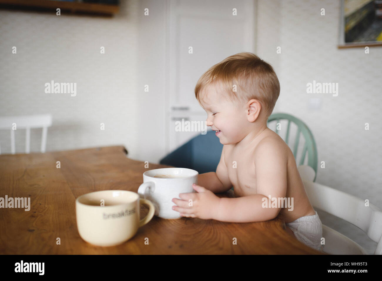 Lachen kleiner Junge am Küchentisch holding Schale sitzen Stockfoto