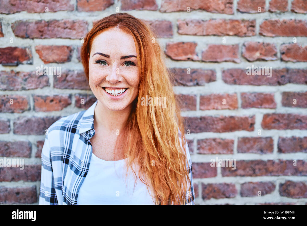 Porträt der schönen jungen Frau an der Kamera vor der Mauer lächelnd Stockfoto