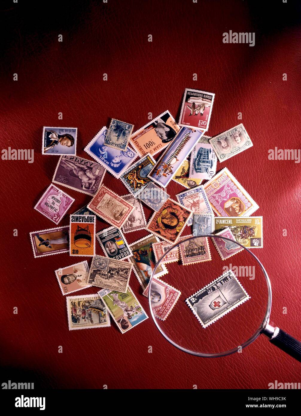Eine Reihe von Briefmarken aus der ganzen Welt zufällig in einem Haufen mit einer Lupe auf einem roten Hintergrund gestapelt. Stockfoto