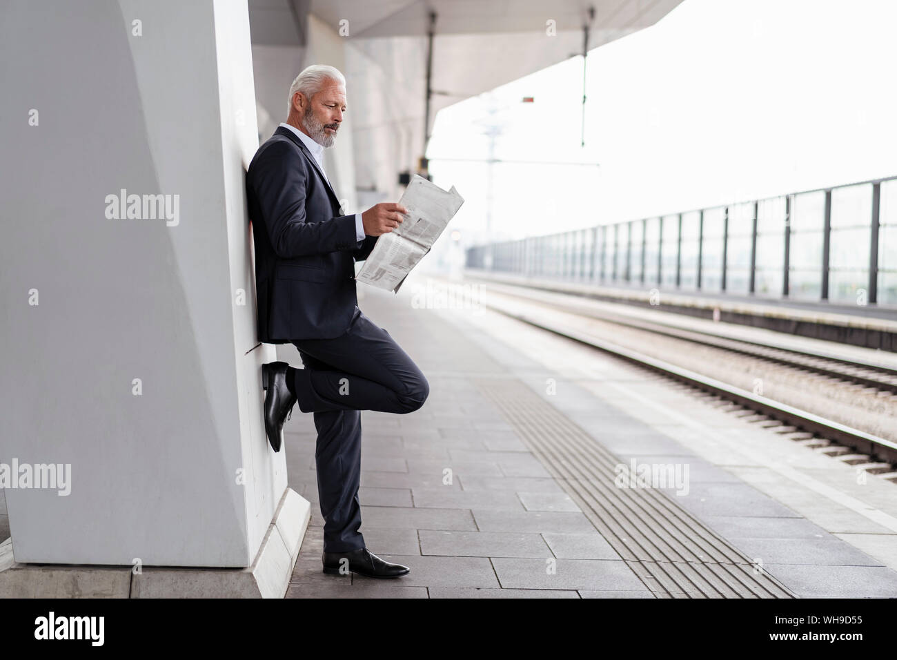 Reifen Geschäftsmann lesen Zeitung, die sich am Bahnsteig Stockfoto