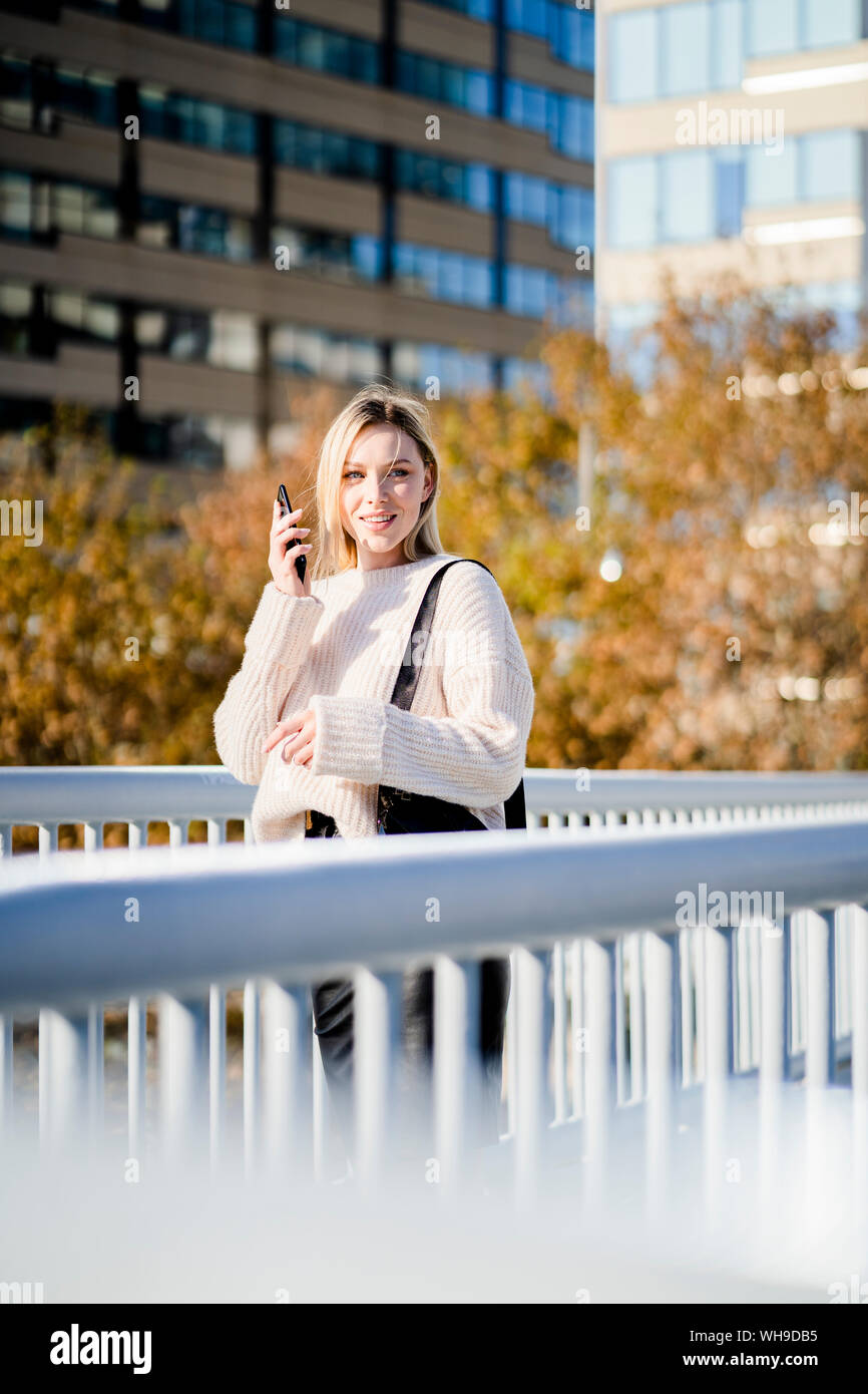 Portrait von lächelnden jungen Frau mit Smartphone auf der Fußgängerbrücke im Herbst Stockfoto
