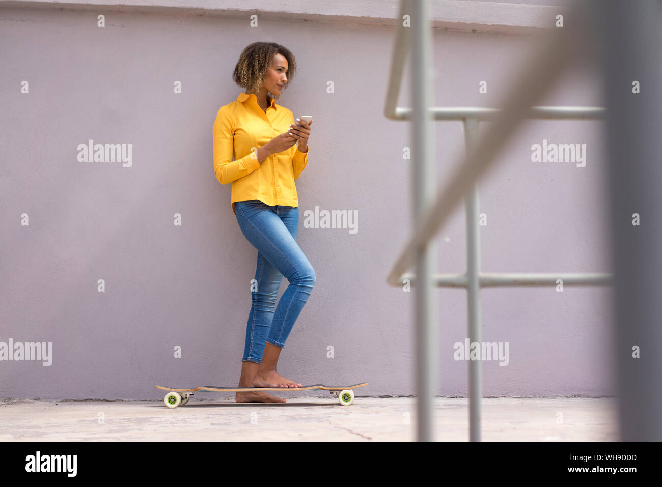 Jungen barfuß Frau mit Smartphone und Skateboard tragen gelbe Shirt und Jeans Stockfoto