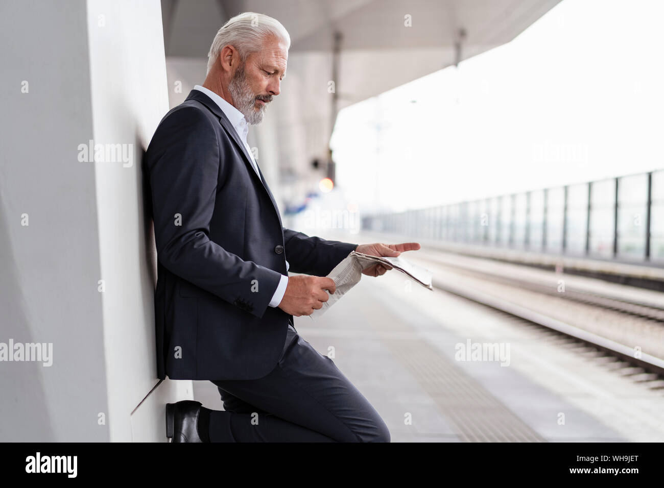 Reifen Geschäftsmann lesen Zeitung, die sich am Bahnsteig Stockfoto