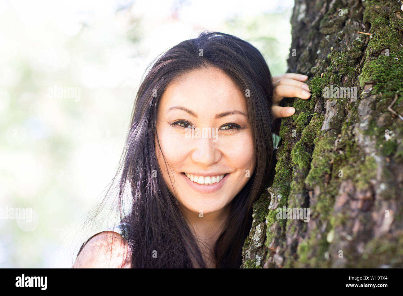Portrait einer jungen lächelnde Frau an einen Baumstamm gelehnt Stockfoto