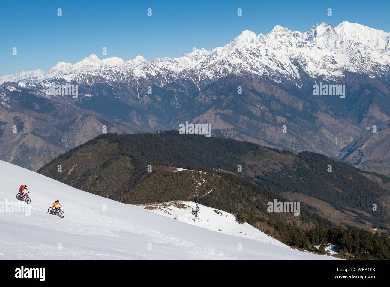 Mountainbiker fahren auf einem schneebedeckten Hang in der Himalaya mit Blick auf den Langtang Bereich in der Ferne, Nepal, Asien Stockfoto