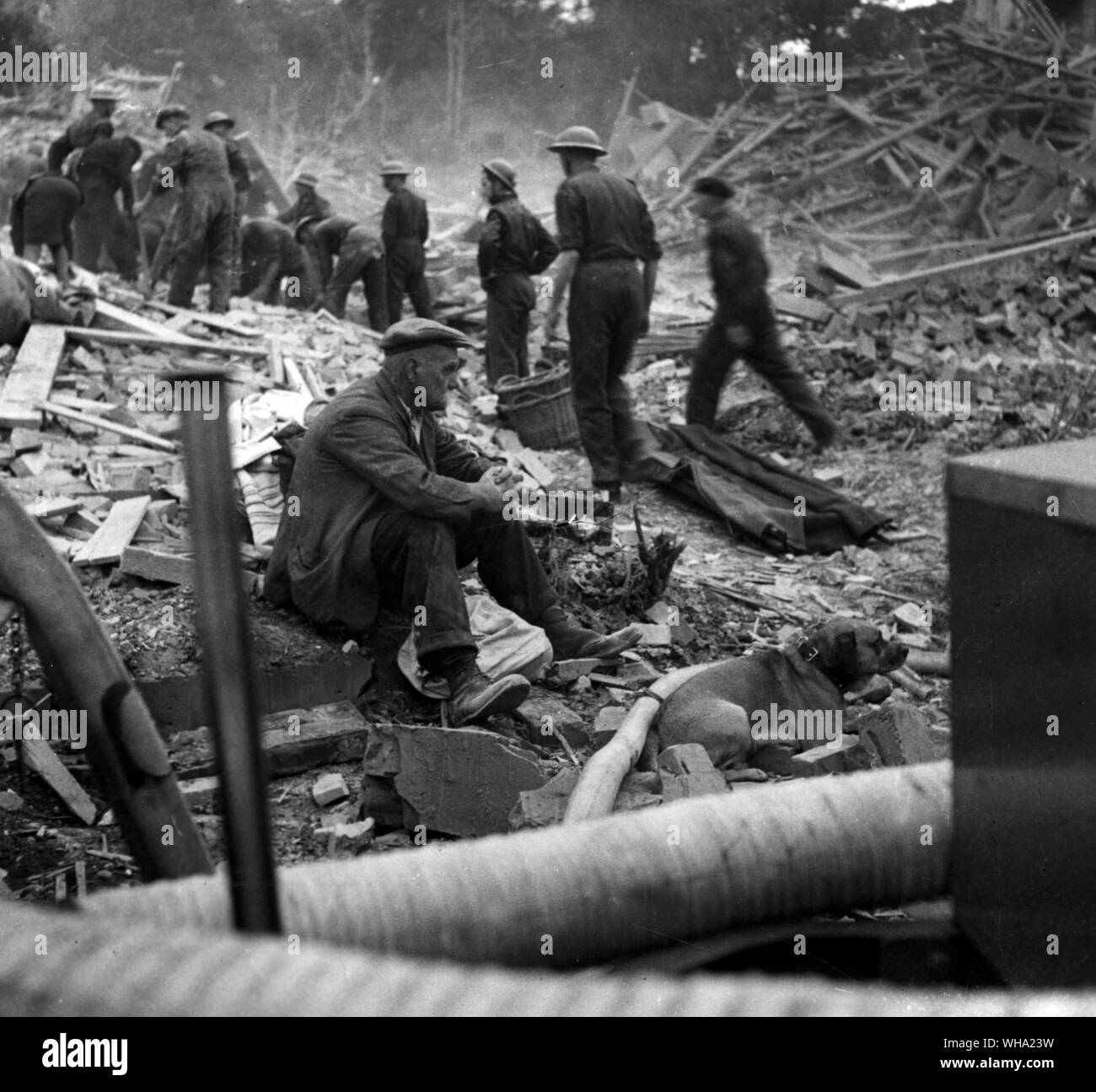 WW2: Ältere Opfer eines Bombenangriffs. Er hatte gerade seinen Hund für einen Spaziergang, aber wenn Auf der Rückkehr aus, er sein Haus in Trümmern und seine Frau tot aufgefunden. Zivilschutz Arbeiter im Hintergrund. Stockfoto
