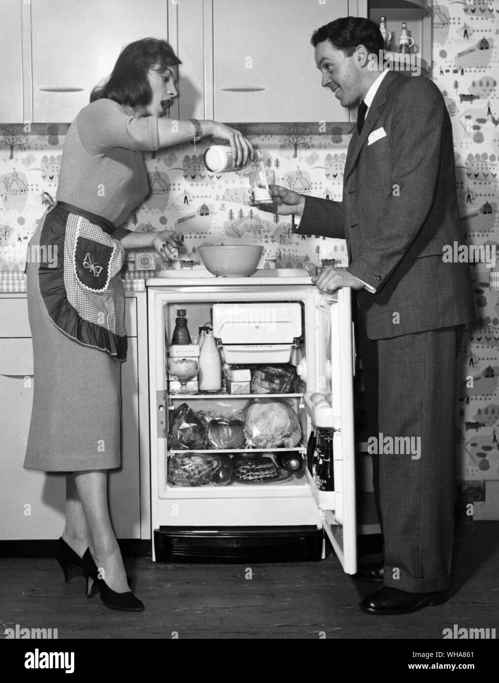 Frau gießt ein Glas Milch für einen Mann. Kalte Milch aus dem Kühlschrank Stockfoto
