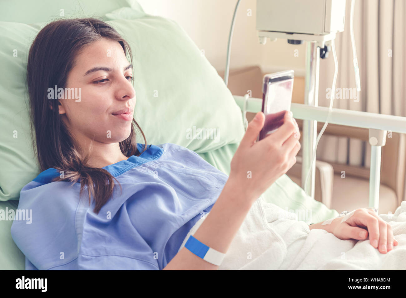 Schöne junge Patienten Frauen im Krankenhaus Bett lag, und lächelnd mit Smart Handy während der Genesung im Krankenhaus. die Wiederherstellung von Patienten Frauen sind ha Stockfoto
