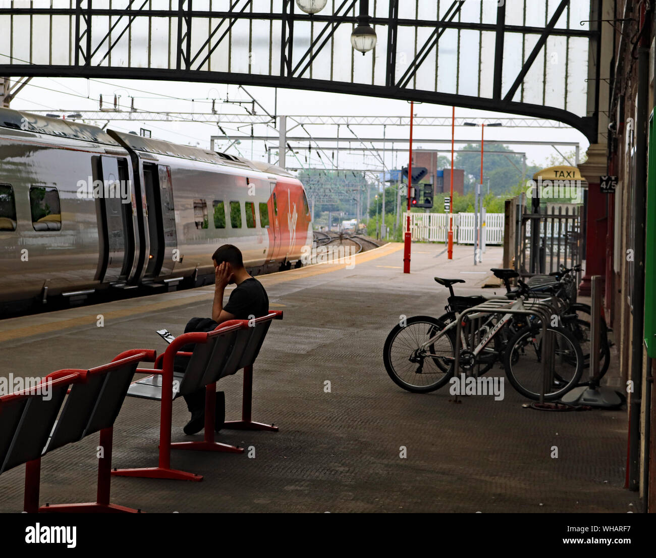 Eine Jungfrau Zug steht in Stoke on Trent Bahnhof bilden einen Dienst zu London Euston als Passagier Warten auf einen anderen Zug einen Anruf machen Stockfoto