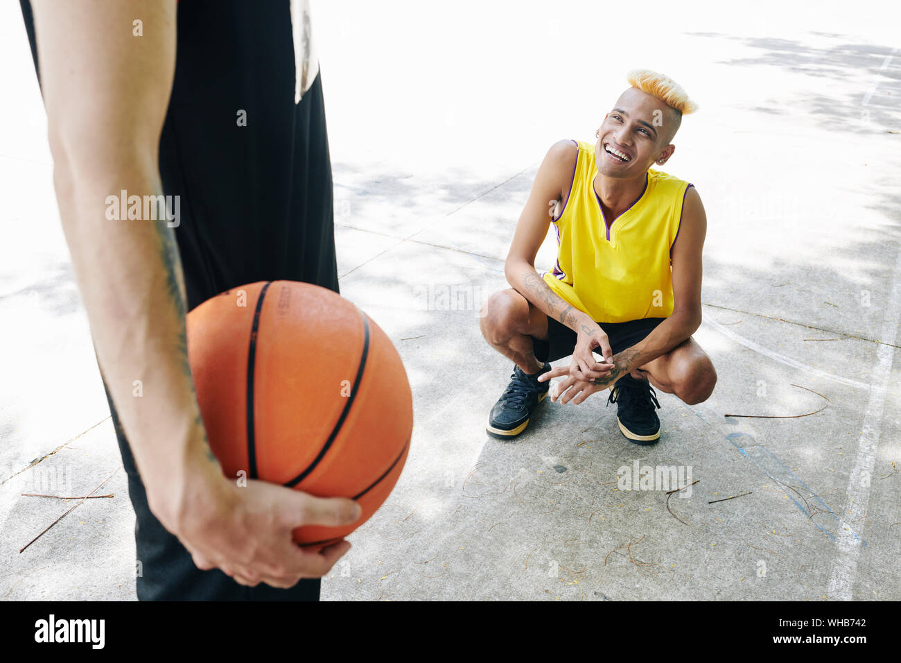 Lächelnden jungen Mann unten crounching und bis auf seine Mannschaftskameraden mit Basketball Ball in Hand Stockfoto