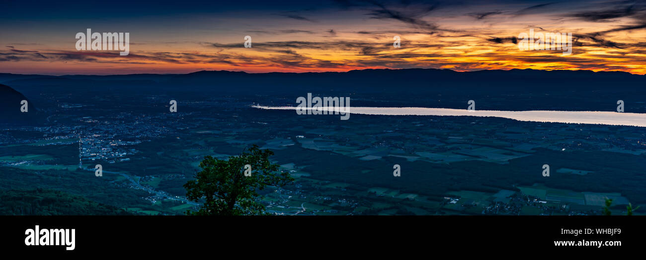 Blick von oben auf das abendliche Panorama, der Schweiz, Frankreich und den Genfer See auf dem Hintergrund der Konturen der Berge mit Orange Sky. Stockfoto