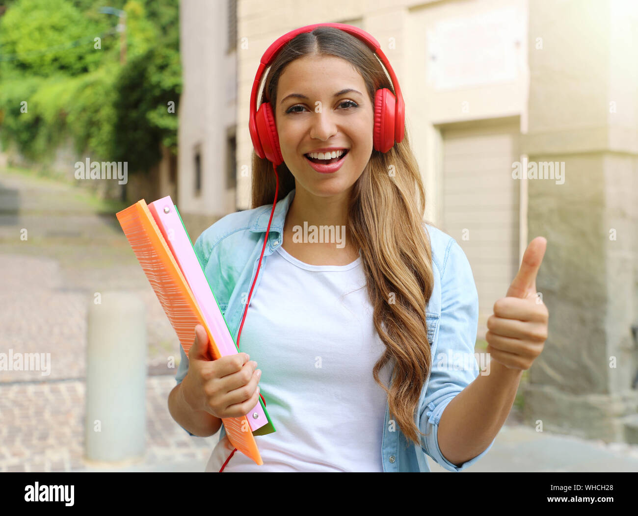 Glückliche Schüler Mädchen mit Kopfhörer gibt Daumen hoch, im Freien. Junge Frau, Student Exchange Programm. Stockfoto