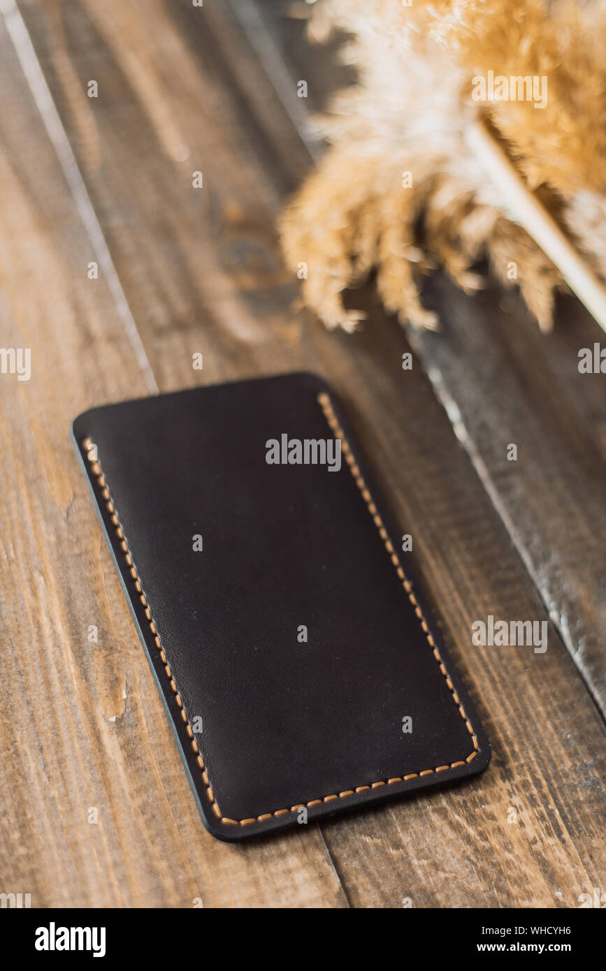 Teuer, schönes Cover von eco-Leder auf einem Hintergrund von Holz und Weizen. Schöne Natur Care Concept. Handgefertigte Phone Case in der Farbe schwarz. Stockfoto