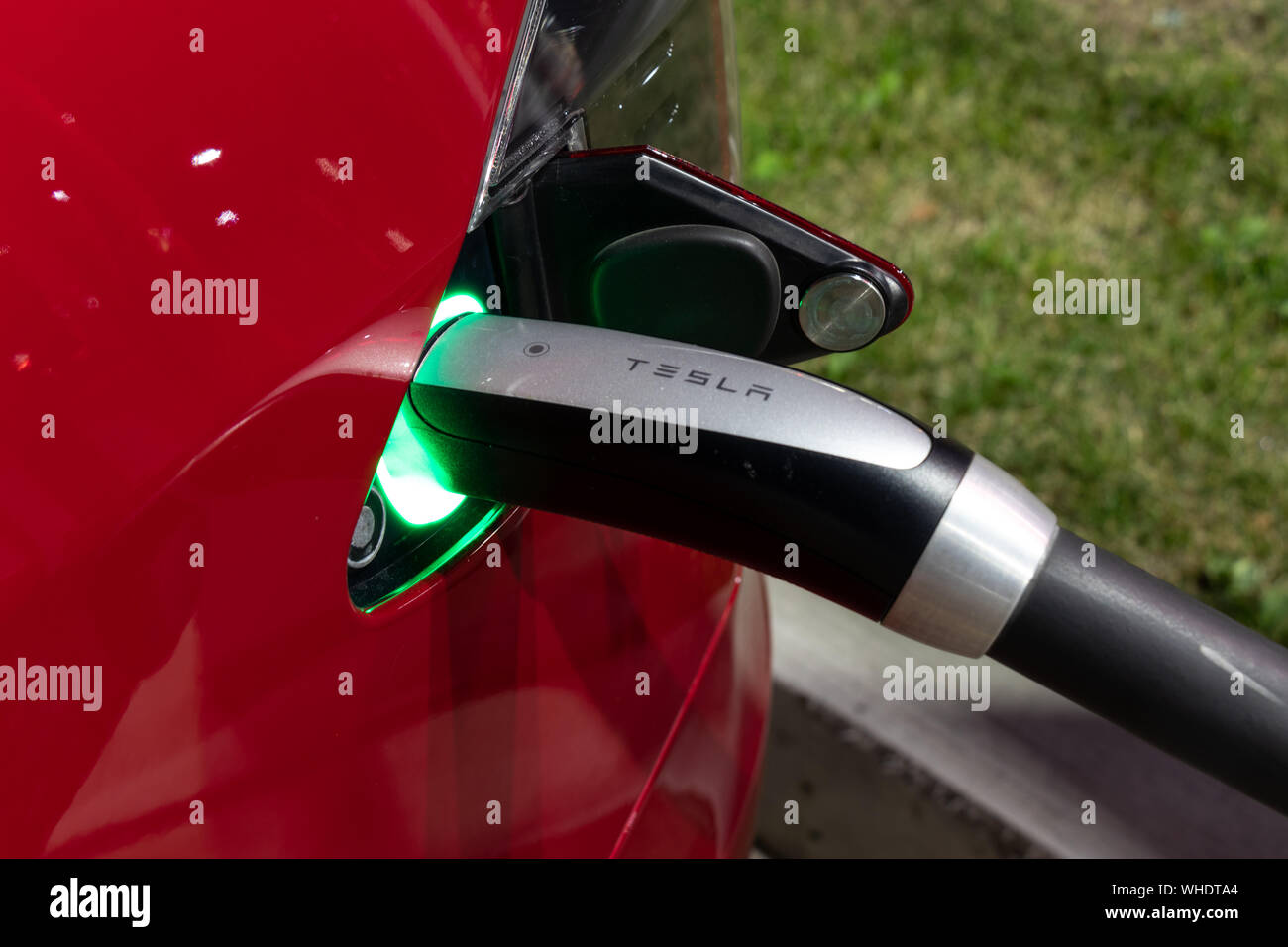 Tesla Supercharging Kabelgriff gesehen, während angeschlossen an roten Tesla in der Nacht. Stockfoto