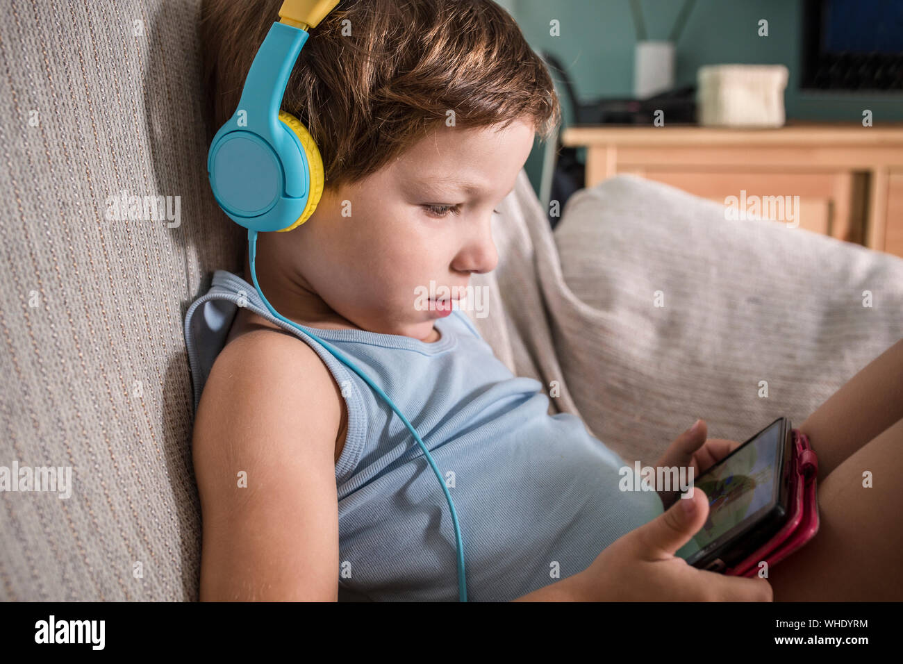 4 Jahre Junge in Kopfhörer Videos mit Smartphone. Sie sitzen auf dem Sofa im Wohnzimmer zu Hause Stockfoto