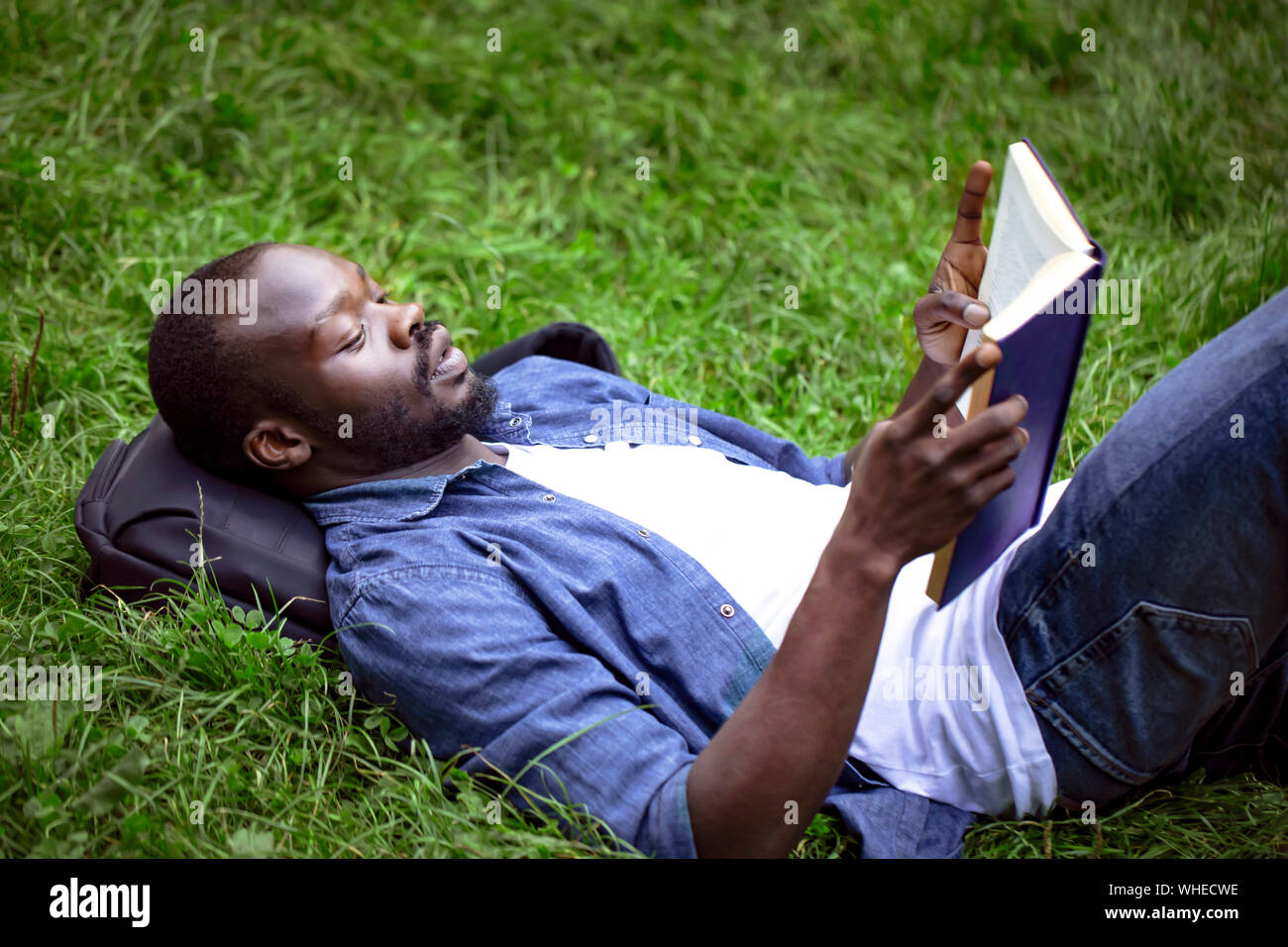 Schwarze männliche Schüler lesen ein Lehrbuch liegen auf einem Campus Rasen konzentriert Stockfoto