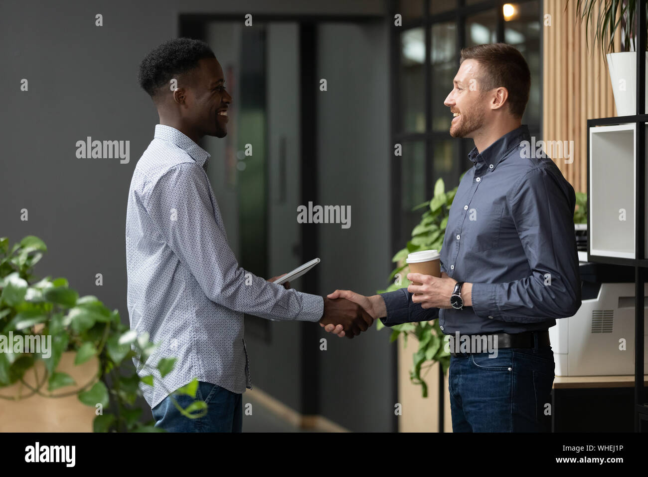 Zwei glückliche diverse männliche Kollegen handshaking stehen in modernen Büro Stockfoto