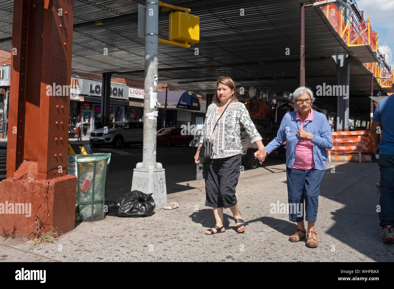 Zwei Frauen, anscheinend Mutter & Tochter, gehen Hand in Hand unter dem erhöhten U-Bahn auf Roosevelt Ave. in Jackson Heights, Queens, New York City. Stockfoto