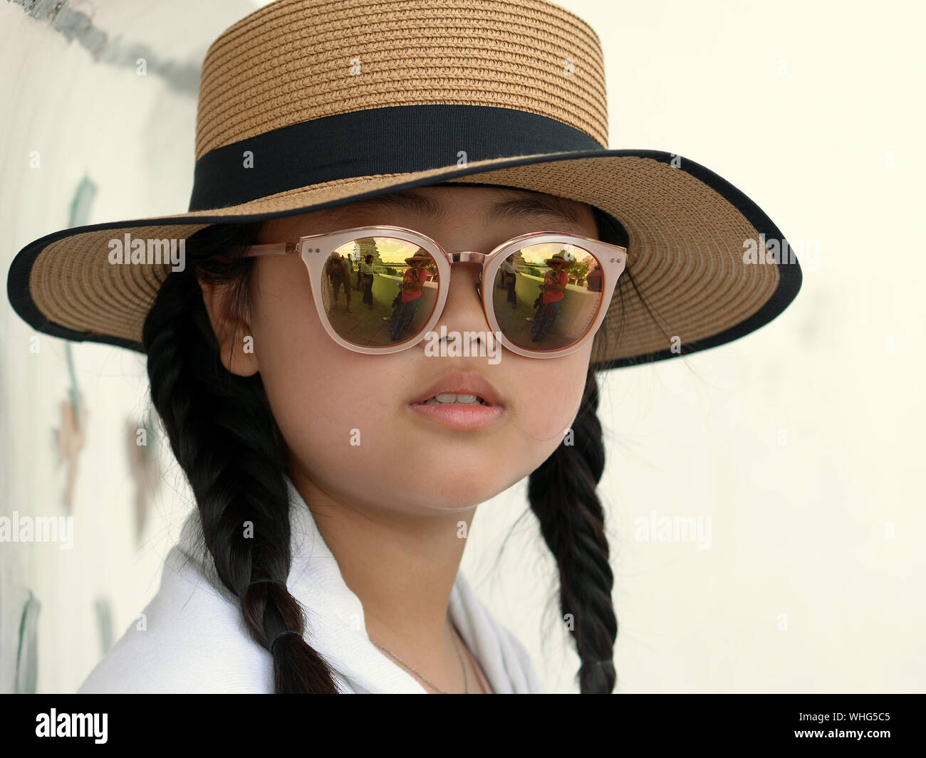 Süße Thai vor - jugendlich Mädchen mit Zöpfen, verspiegelte Sonnenbrille und ein modernes Strohhut posiert für die Kamera. Stockfoto
