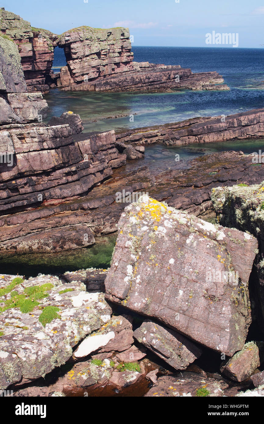 Blick über das Meer zu einem Natural Arch und Felsen in der Nähe von Culkein, Sutherland, Schottland mit vielen natürlichen Farben im Meer und auf die Felsen Stockfoto