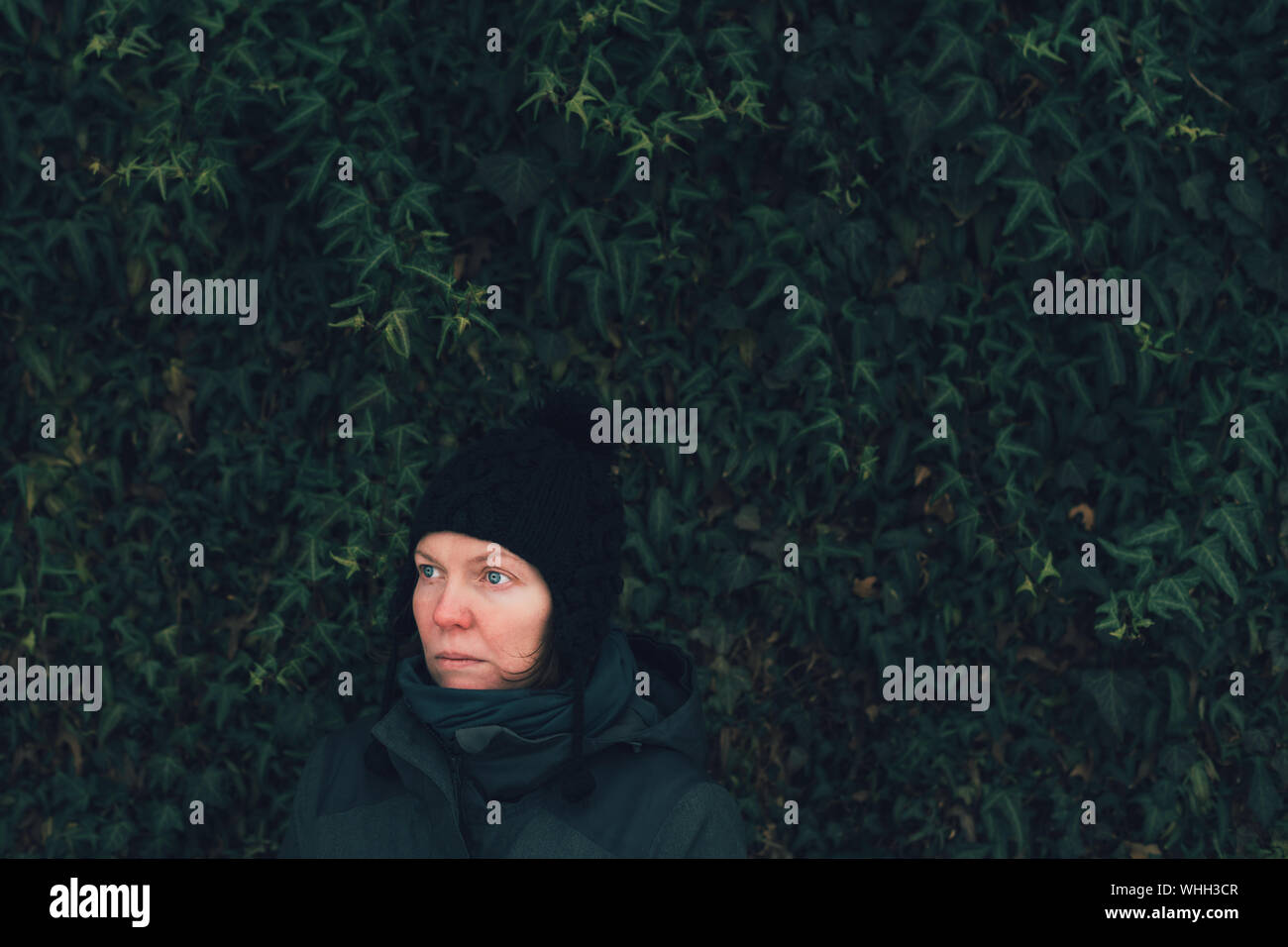 Schwere Frau im Winter Kleidung gegen die ivy Wand om kalten Wintertag, traurig und besorgt Stockfoto