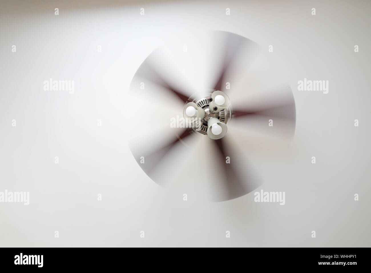 Ein Deckenventilator auf einer weißen Decke, in der Nähe mit unscharfen Lüfterflügel, drei Lampen, tagsüber. Stockfoto