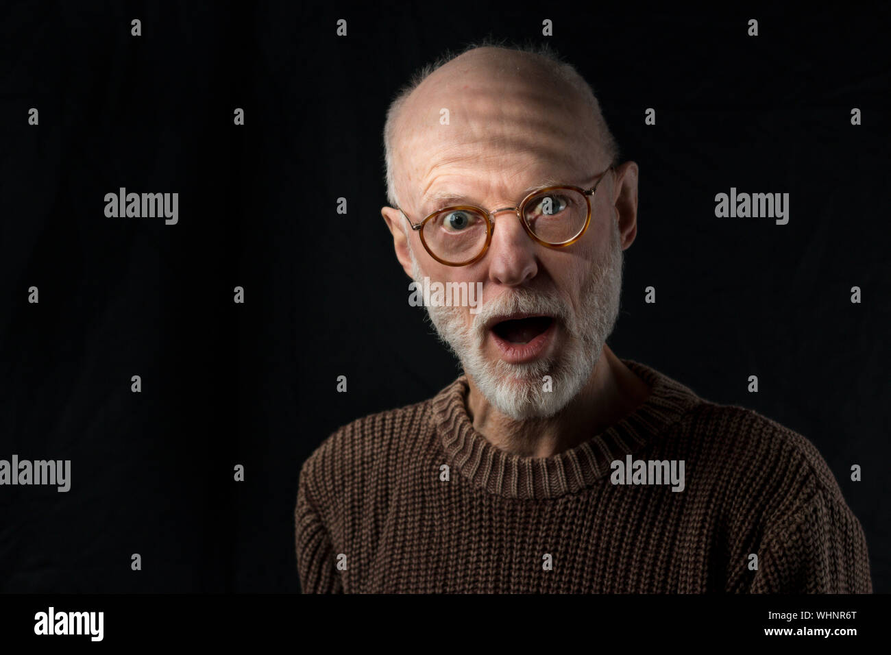 Portrait von Schockierenden älterer Mann mit Pullover auf schwarzem Hintergrund Stockfoto