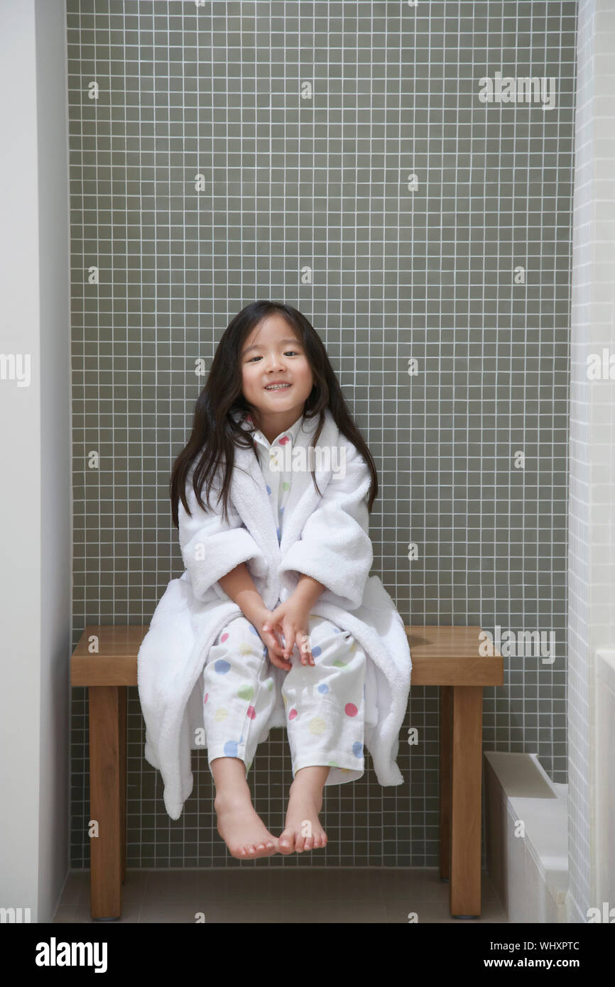 In voller Länge Porträt eines jungen Mädchens in Bademantel sitzt auf der Bank durch die Badewanne Stockfoto