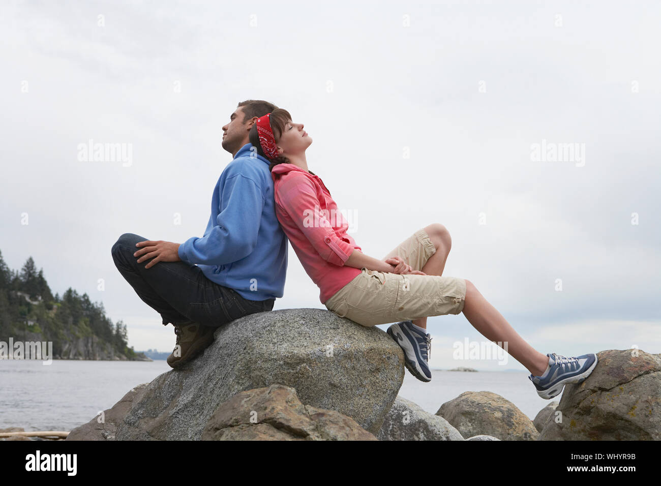 Volle Länge Seitenansicht eines jungen Paares zurück sitzen auf den Felsen gegen Ozean zurück Stockfoto