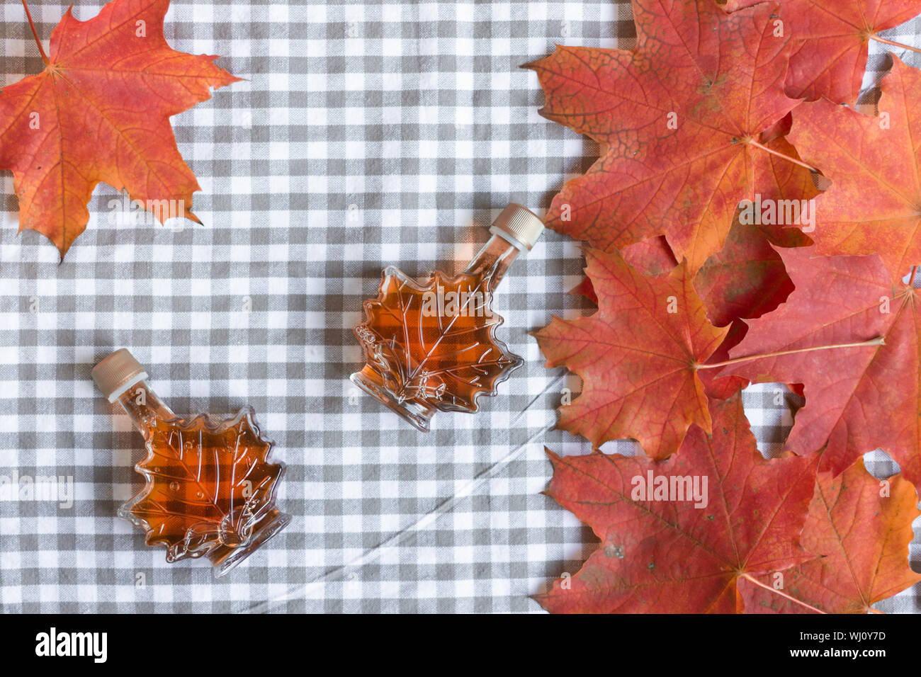 Ahornsirup in einer Flasche in einer Form der Maple Leaf. Red maple leaf Hintergrund. Stockfoto