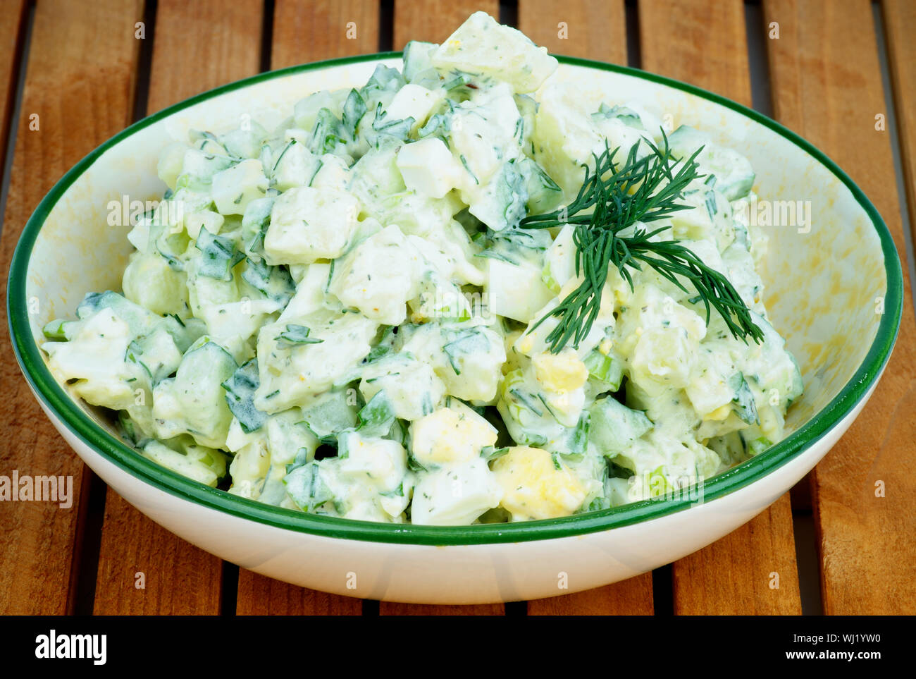 Köstliche Frisch zubereitete Cremige Kartoffel Salat garniert mit Dill in Beige Schüssel closeup auf Holzbrett Hintergrund Stockfoto