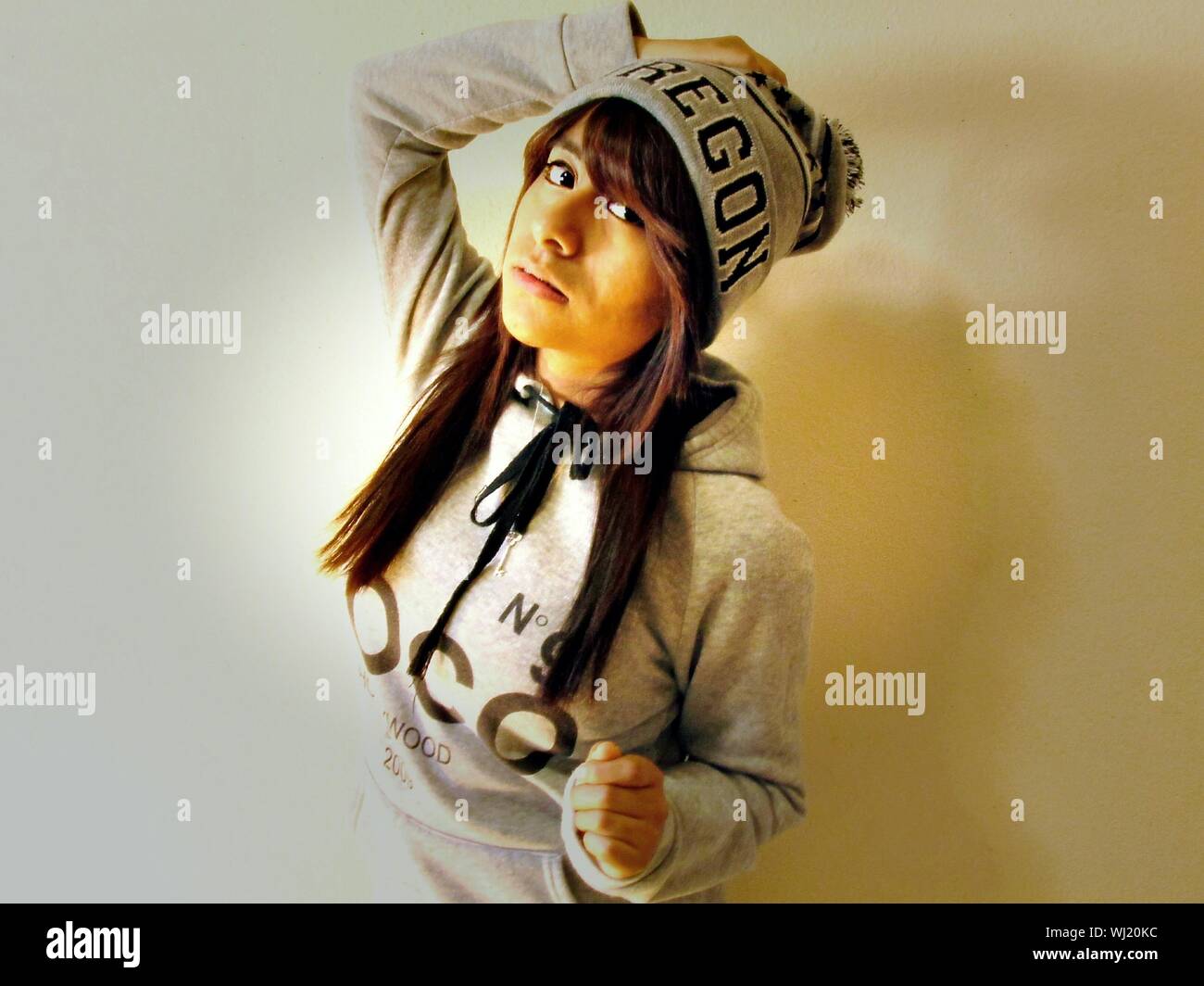 Junge Frau mit der Hand auf dem Kopf stehend gegen Wand Stockfoto