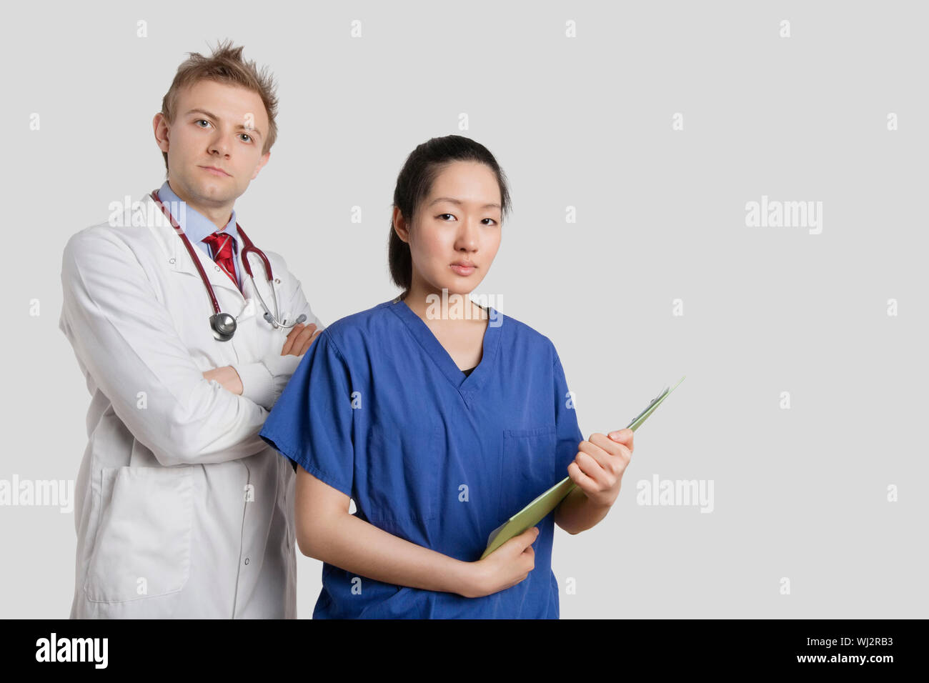 Porträt eines kaukasischen Arztes stehend mit einer asiatische Krankenschwester über grauen Hintergrund Stockfoto