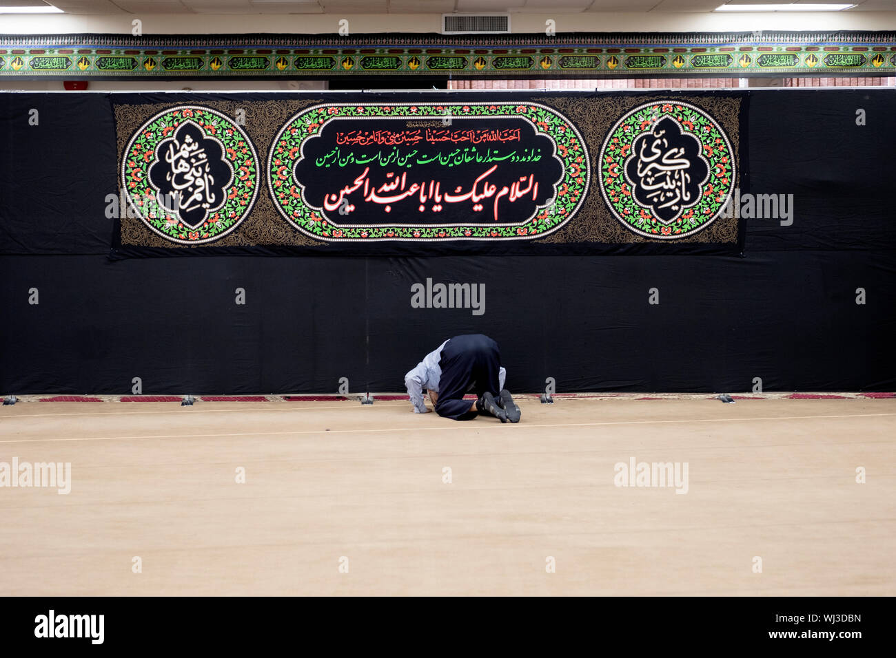Ein gläubiger Muslim mann Bögen im Gebet vor der Koran Zitate an der Imam Al-Khoei Islamische Zentrum in Jamaica, Queens, New York City Stockfoto