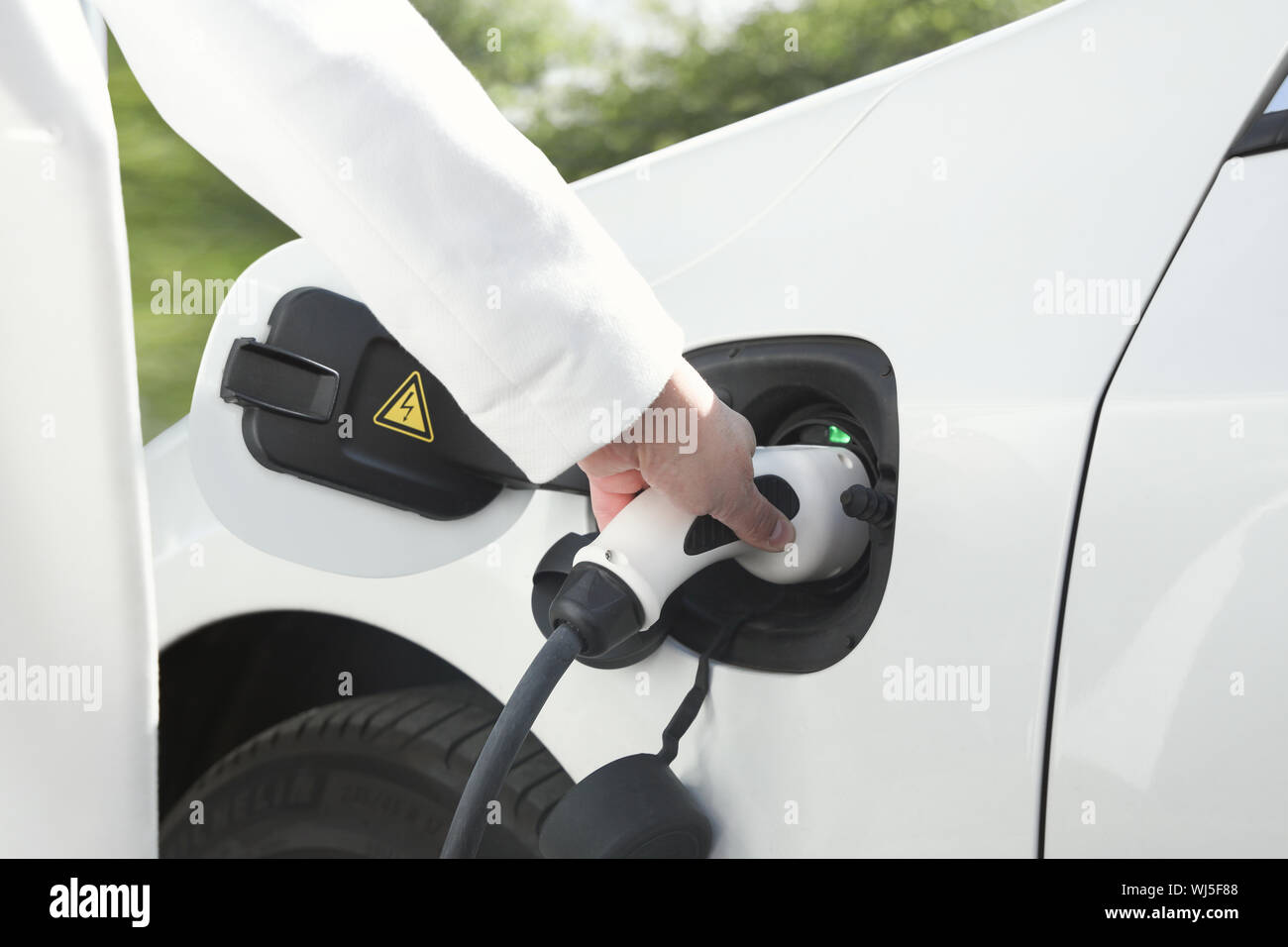 Weibliche Hand, die eine elektrische Stecker zum Aufladen von Elektroautos oder evt. Umweltfreundliche alternative Energiekonzept grüne Umgebung. Stockfoto