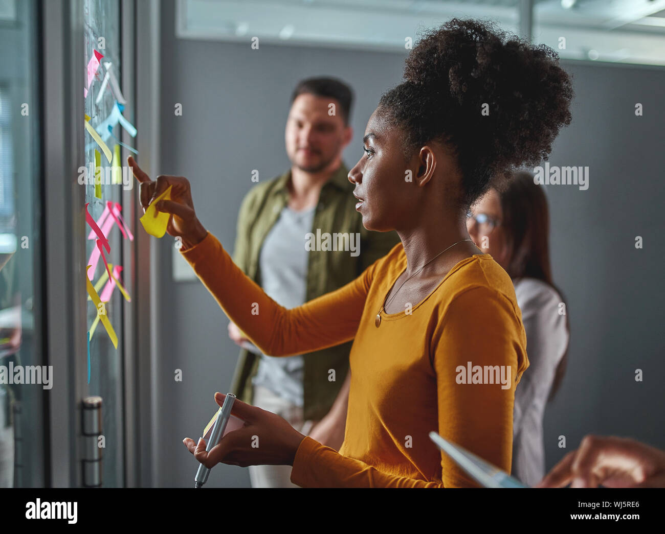 Seitenansicht eines jungen afrikanischen Geschäftsfrau, die Überprüfung und das Festhalten Hinweise auf Glas in der Sitzung in modernen Büro Stockfoto