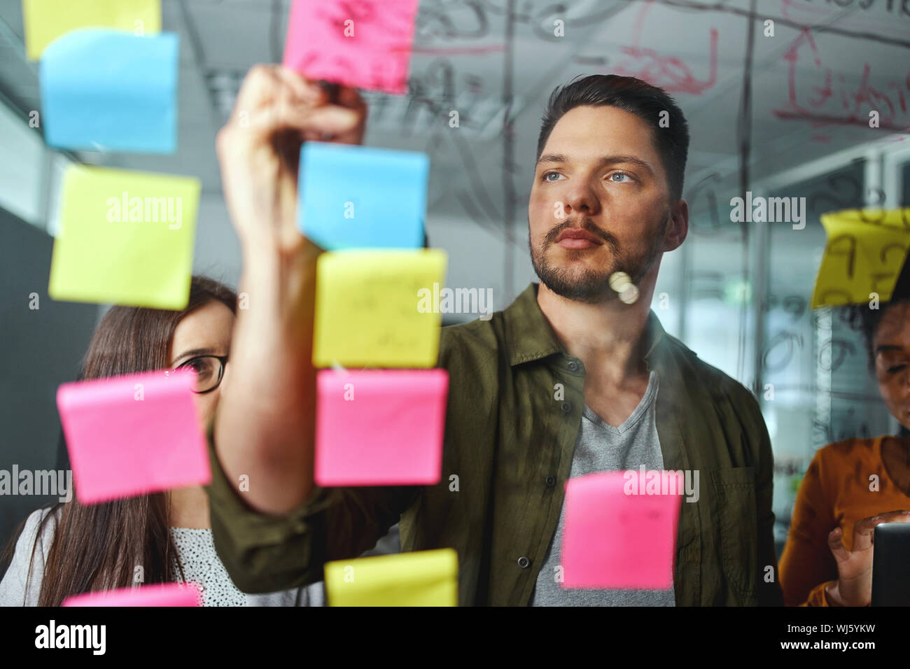 Geballte männliche executive Diskussion von Ideen mit Kollegen durch Schreiben auf Haftnotizen über das Glas board eingefügt Stockfoto