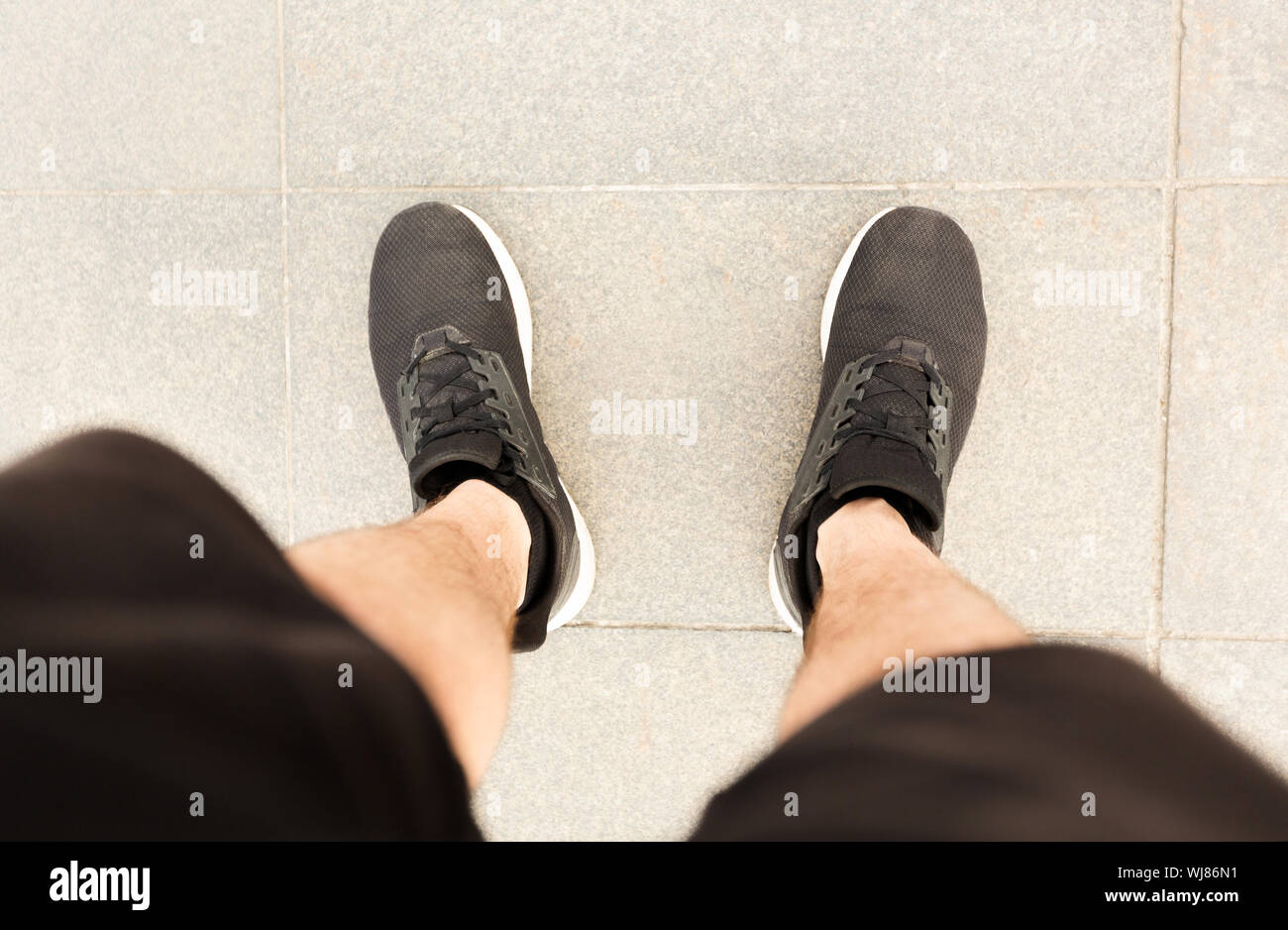 Blick von oben auf die Beine in schwarzen Sneakers auf Betonboden Stockfoto